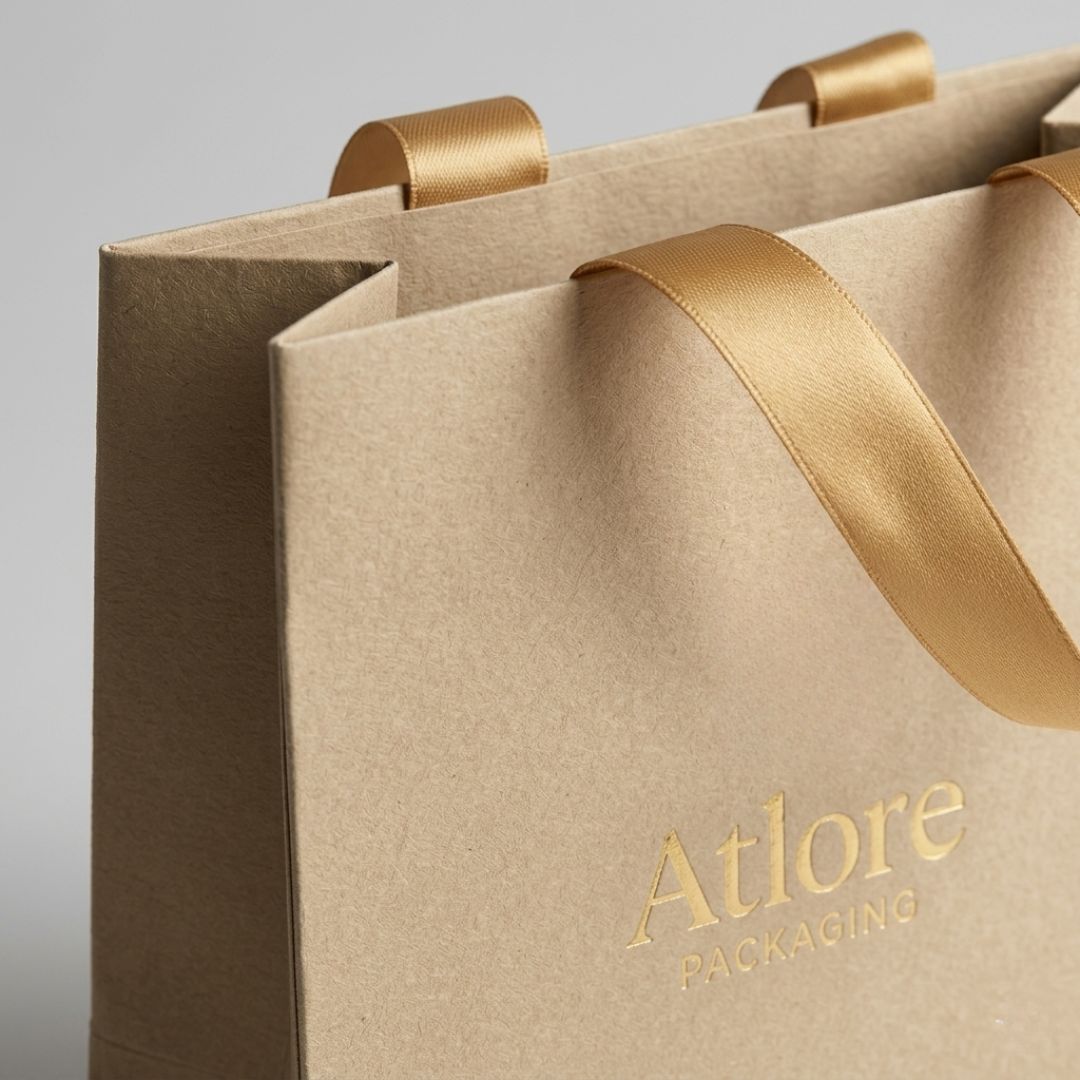 Macro close-up of a reinforced top rim and gold foil logo embossing on a warm beige luxury paper packaging bag.