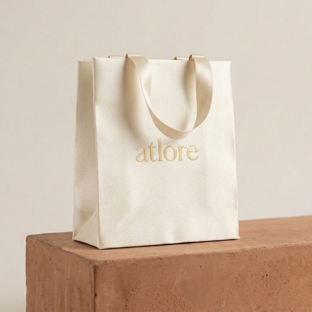 Custom branded ivory satin-coated rigid paper carrier bag with printed logo for luxury bridal jewelry house packaging.