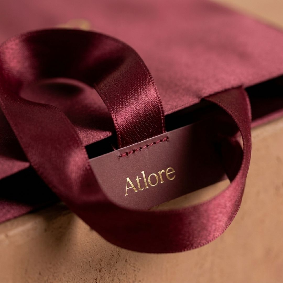 Detailed macro view of a satin ribbon handle and the fabric-coated paper seam on a maroon luxury packaging carrier.