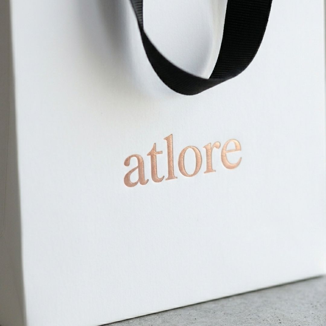 Macro detail of luxury rose gold hot foil stamping on a thick matte coated white card retail jewelry packaging carrier bag.