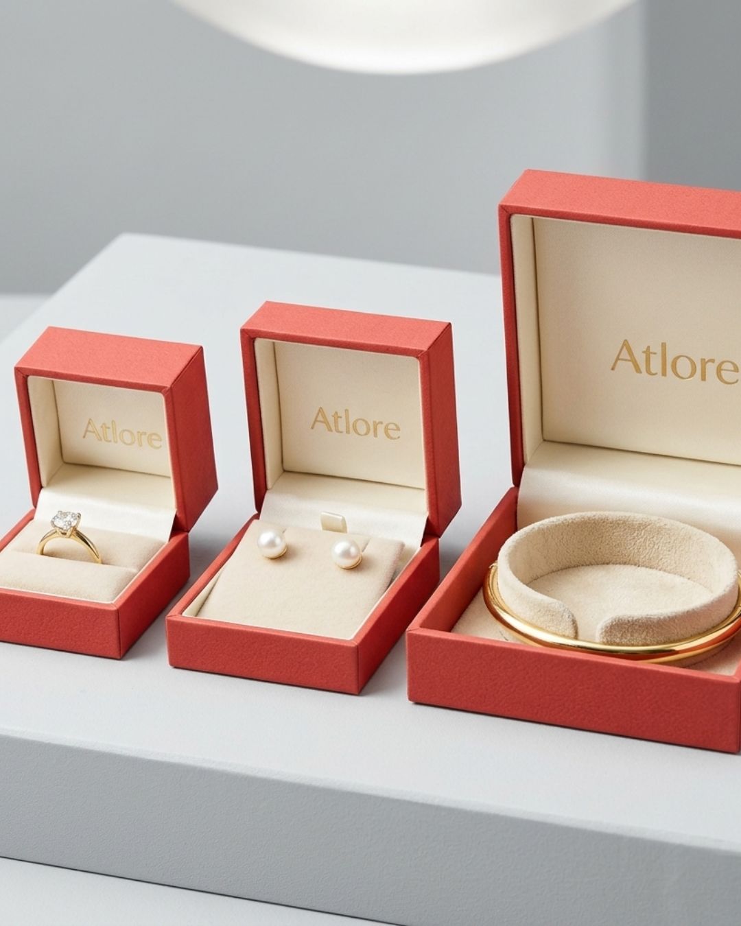A matching trio of custom coral red paper-plastic jewelry packaging boxes lined in cream suede for rings, earrings, and bangles.